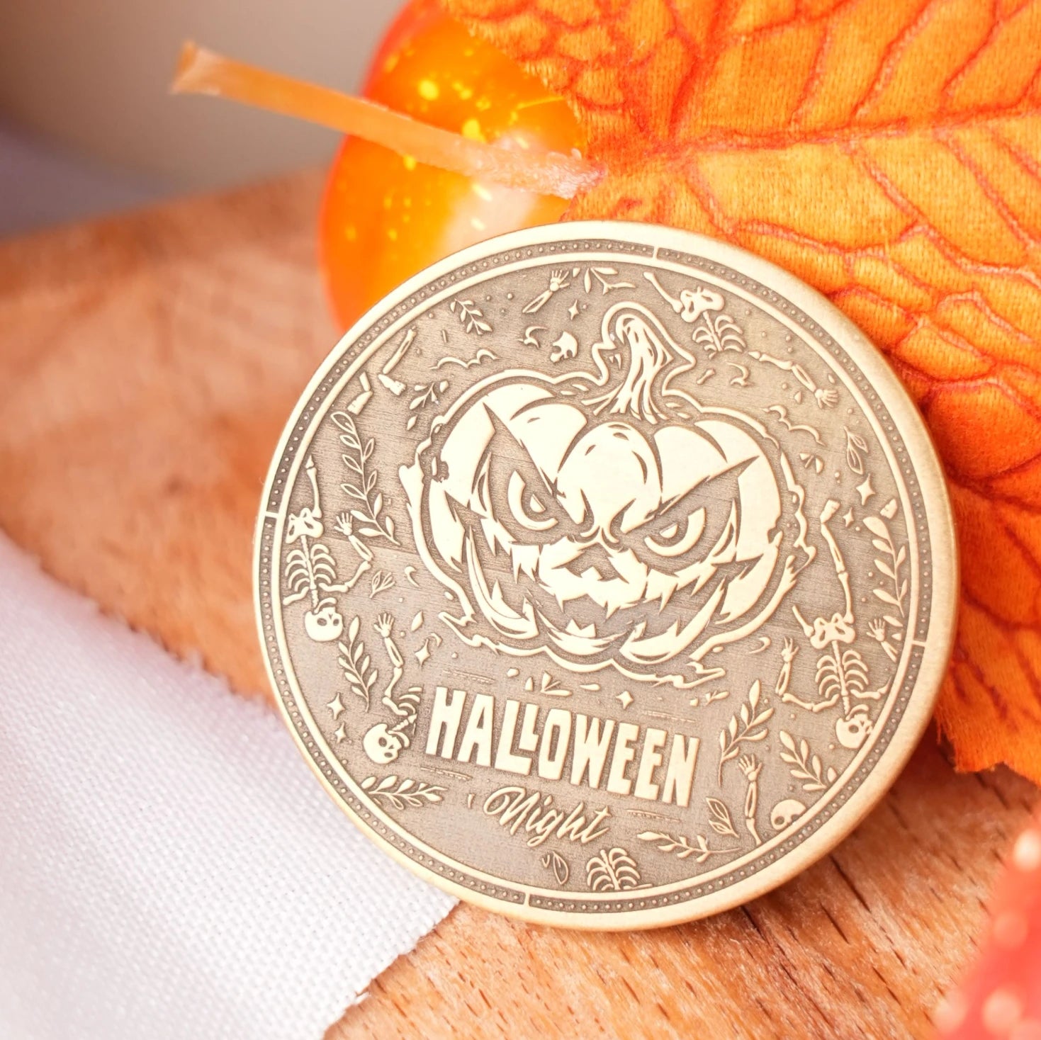 A laser-engraved wooden coin featuring a spooky jack-o'-lantern design and the text "HALLOWEEN Night", surrounded by intricate Halloween-themed patterns like skulls and bats, displayed with a decorative pumpkin candle to highlight its festive application as a custom laser engraving project.