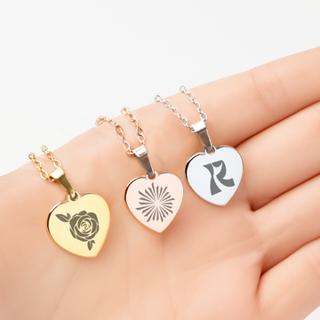 This image showcases three delicate heart-shaped pendant necklaces, each finished in a distinct polished metal and personalized with a unique laser-engraved design: a gold necklace features a classic rose pattern, a rose gold version displays a modern sunburst motif, and a silver pendant bears a stylized initial "R". These customizable pieces exemplify how blank metal jewelry can be transformed into meaningful, one-of-a-kind gifts for special occasions like anniversaries, birthdays, or Valentine’s Day, offe