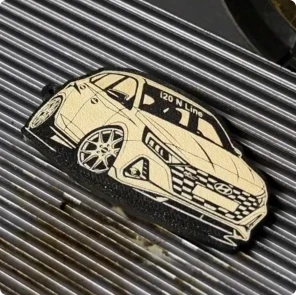 A Maker using a laser engraver to etch a detailed car graphic onto a 3D printed flexible TPU keychain