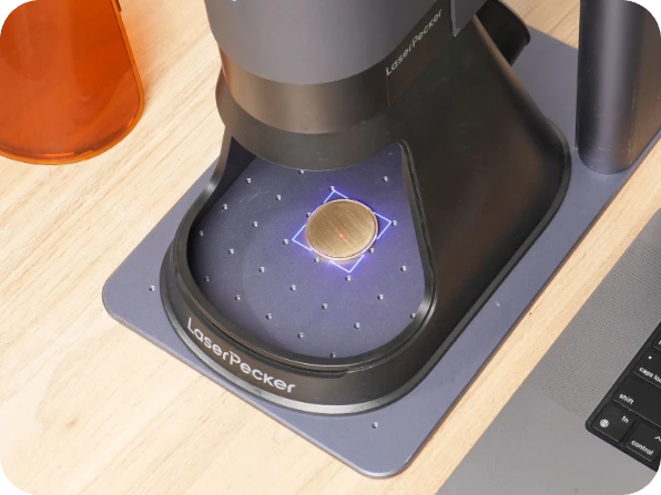 LaserPecker LP5 laser head in preview mode, projecting a blue alignment beam onto a metal coin blank on the LaserPecker mat, demonstrating the real-time preview function of the engraving process.