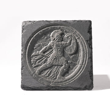 A laser-engraved slate plaque featuring a 3D-style circular design of a classical Greek or Roman warrior, complete with a helmet, shield, and flowing cape. The engraving mimics the texture of ancient stone reliefs, set against the natural rough edges of the slate, creating a durable and historically inspired decorative piece.