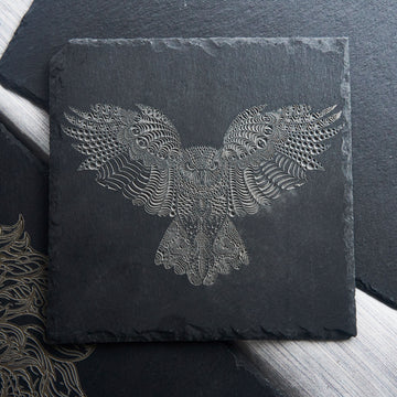 A laser-engraved slate coaster featuring an intricate, abstract eagle design composed of swirling, textured patterns that create a sense of depth and movement. The high-contrast engraving stands out against the dark slate, making it a striking decorative piece or functional drinkware accessory for modern or artistic home decor.
