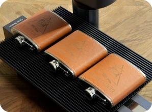 LaserPecker LP2 Plus with slide extension engraving custom monograms on leather flask sleeves, perfect for groomsmen gifts and bar accessories.